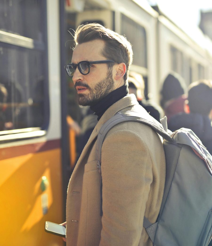 A stylish man with a backpack boards a tram in bustling Budapest, Hungary, during the day.